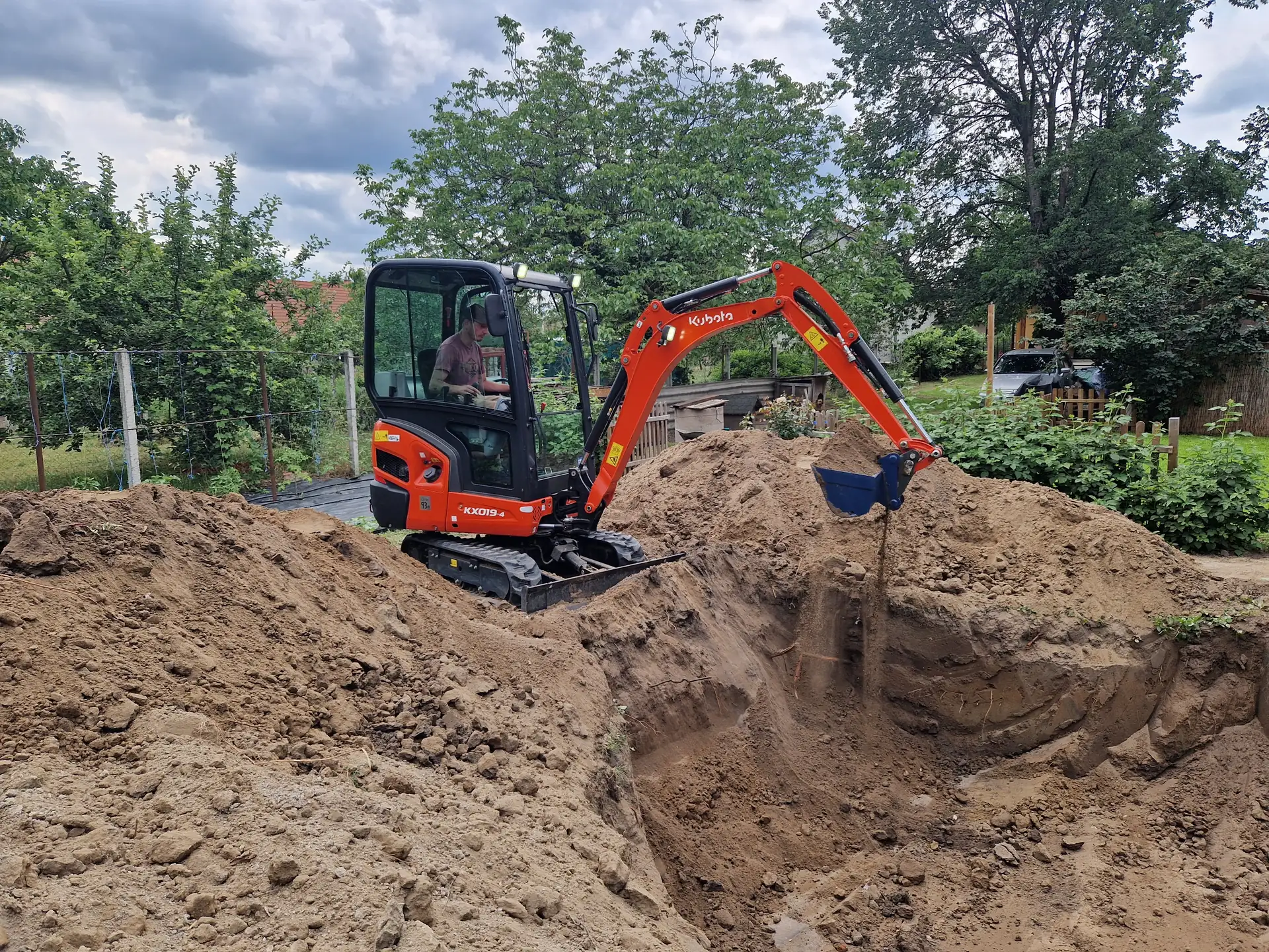 Kubota minikotró gödröt emel ki egy kertben, a kezelő a fülkében